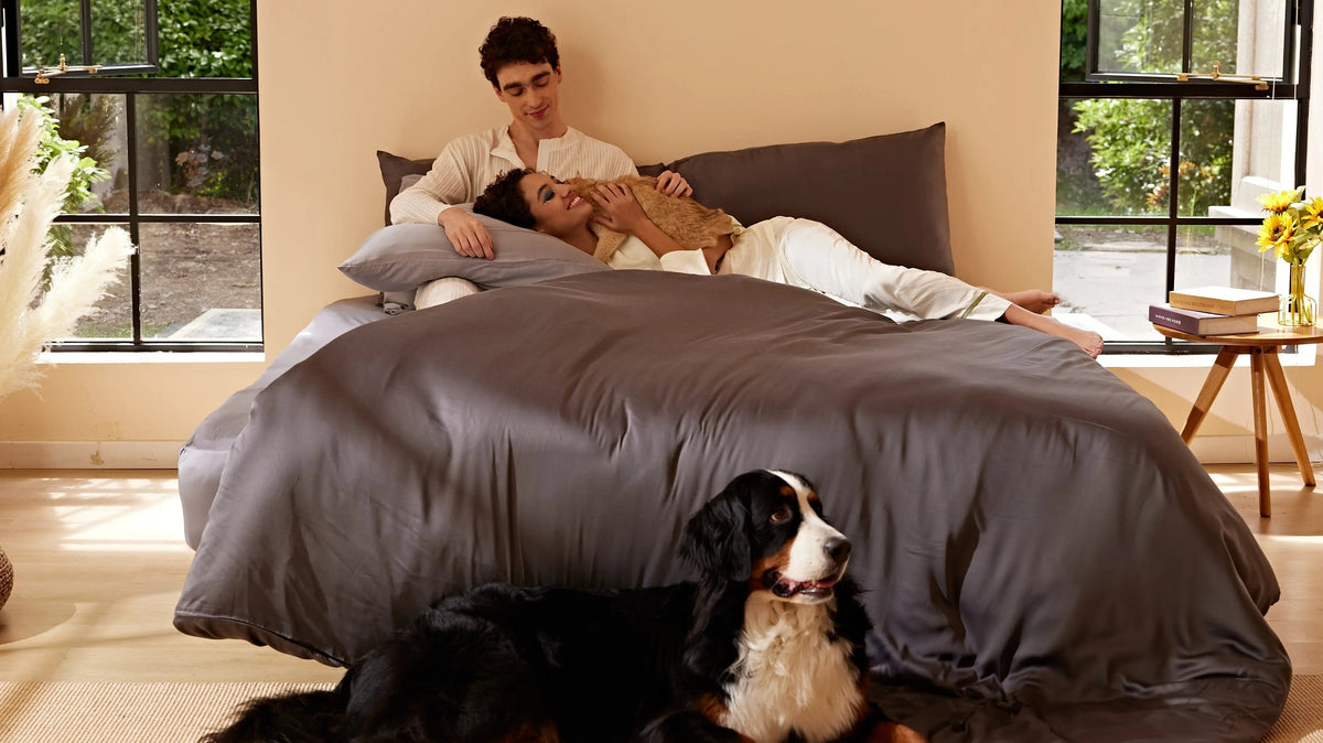 Two people and a cat on gray Furify bedding, with a dog beside the bed