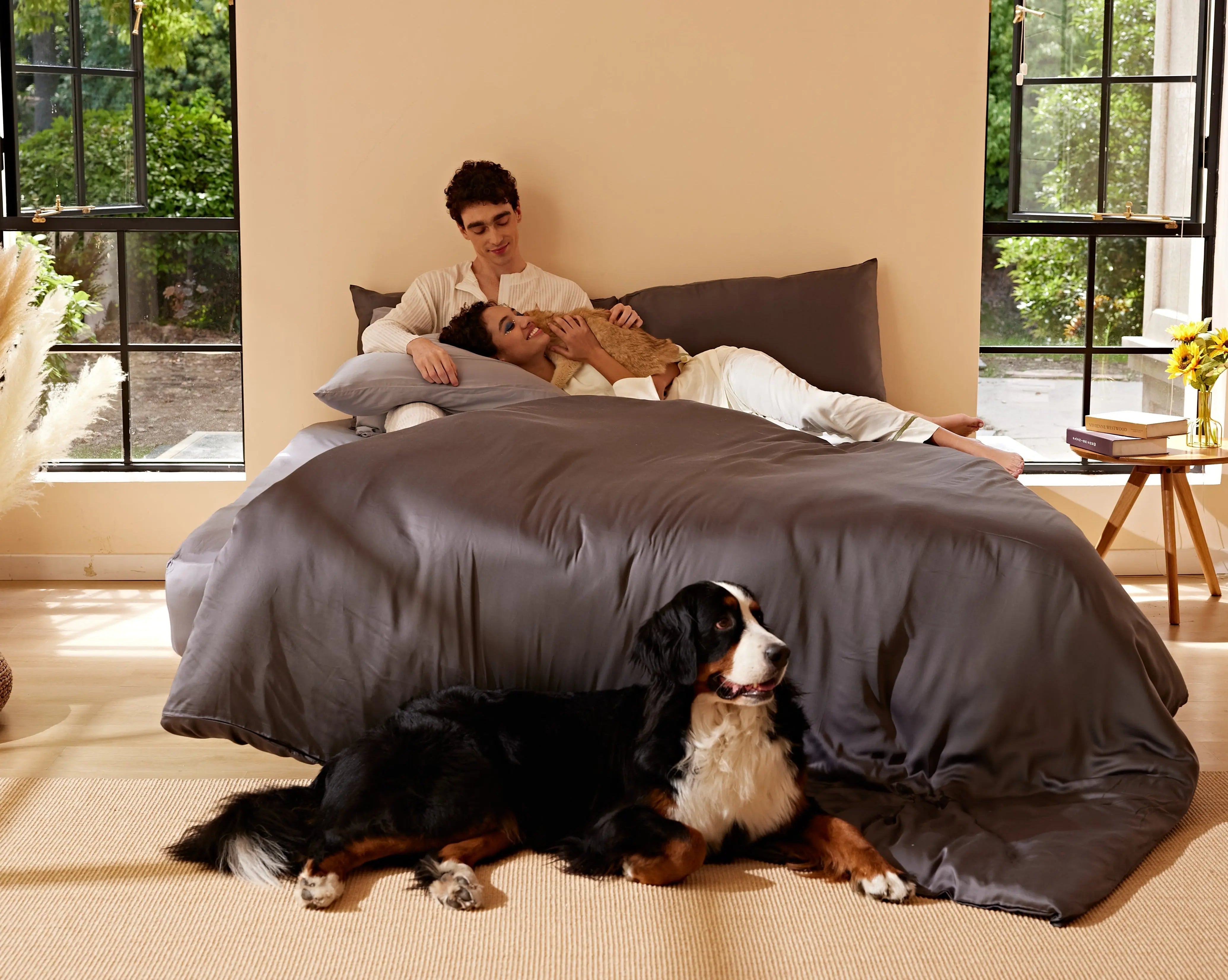 Two people and a cat on gray Furify bedding, with a dog beside the bed